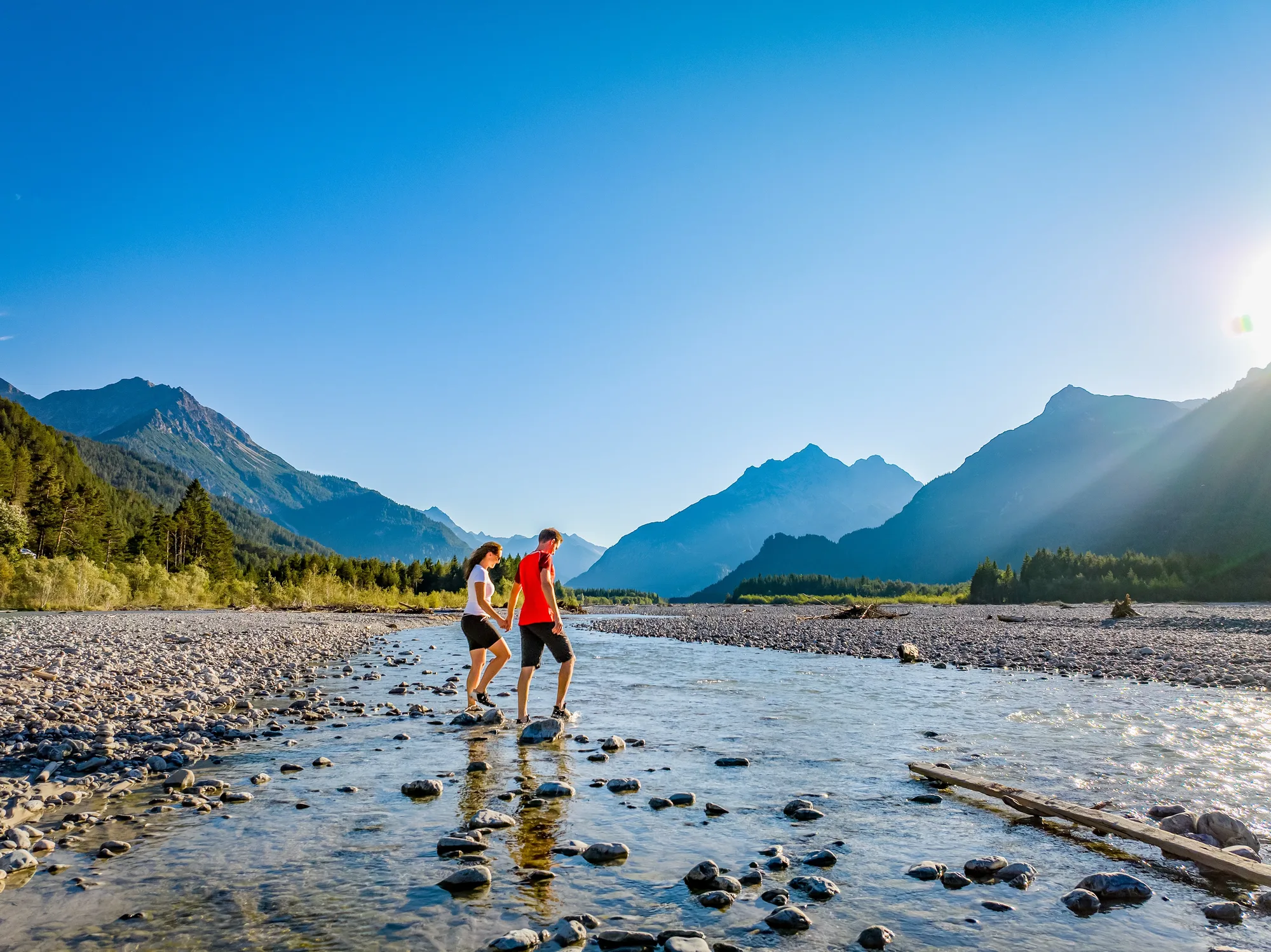 Couple crossing the Lech in summer between mountains and gravel banks